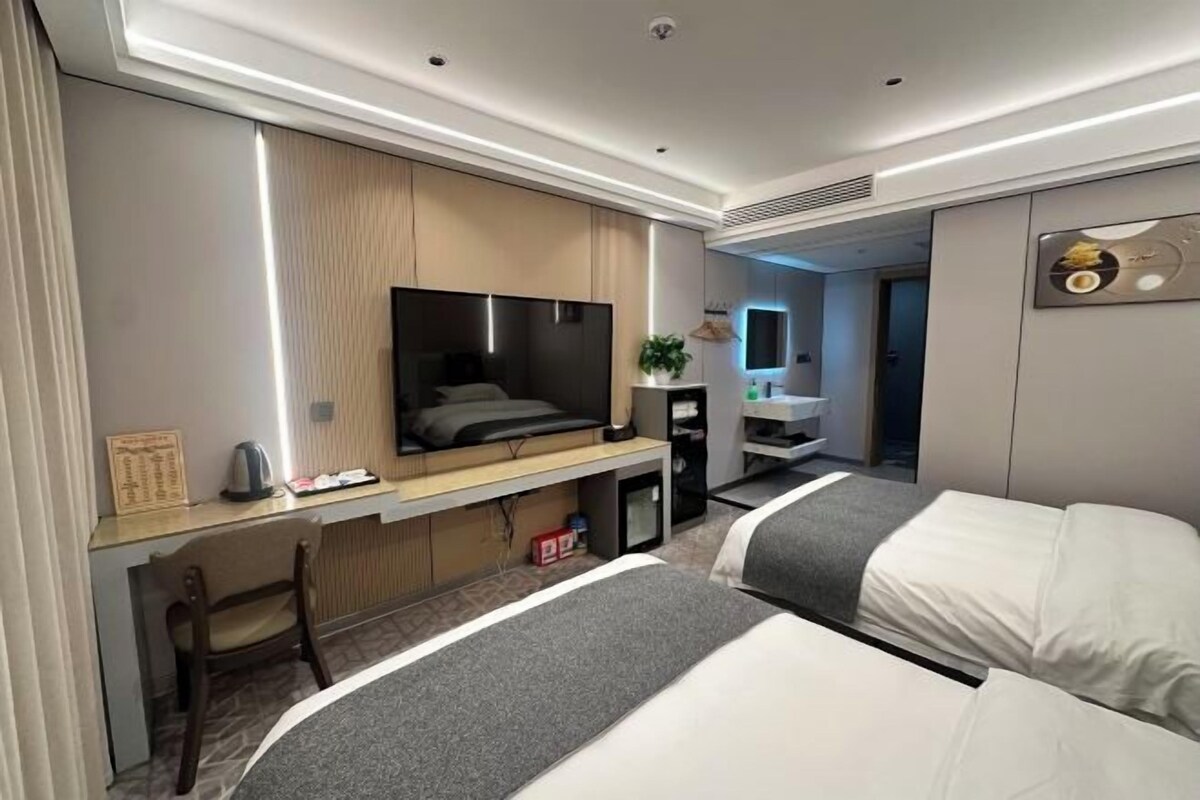 Una habitación de hotel moderna con cama, escritorio, televisor y un baño visible al fondo.