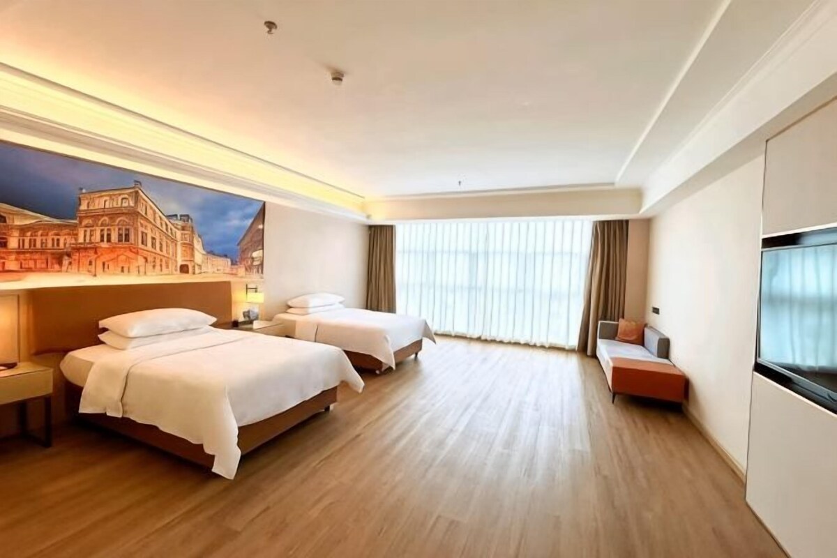A hotel room with two beds, a sofa, a large window, and a cityscape mural on the wall.