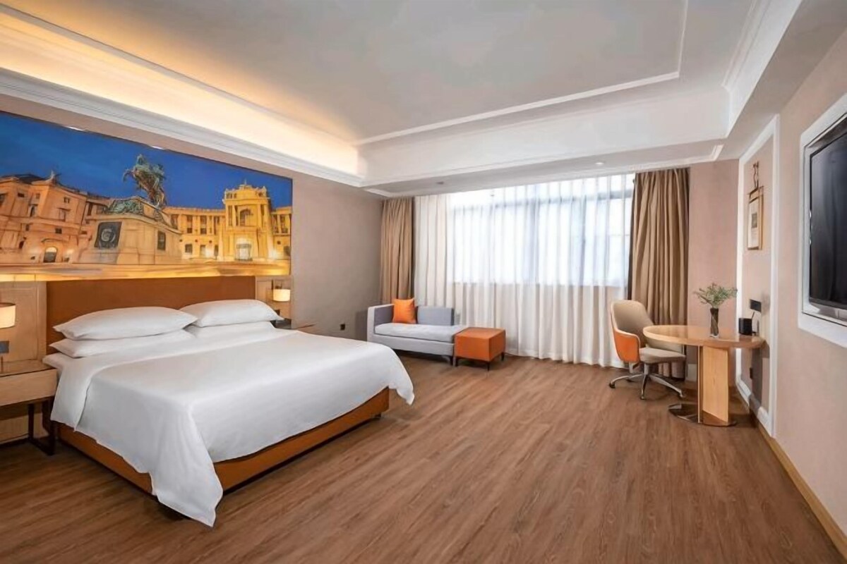 A hotel room with a large bed, a desk, a chair, and a window with curtains.