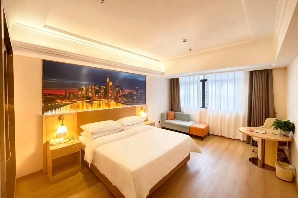 A hotel room with a large bed, a desk, and a view of a cityscape.