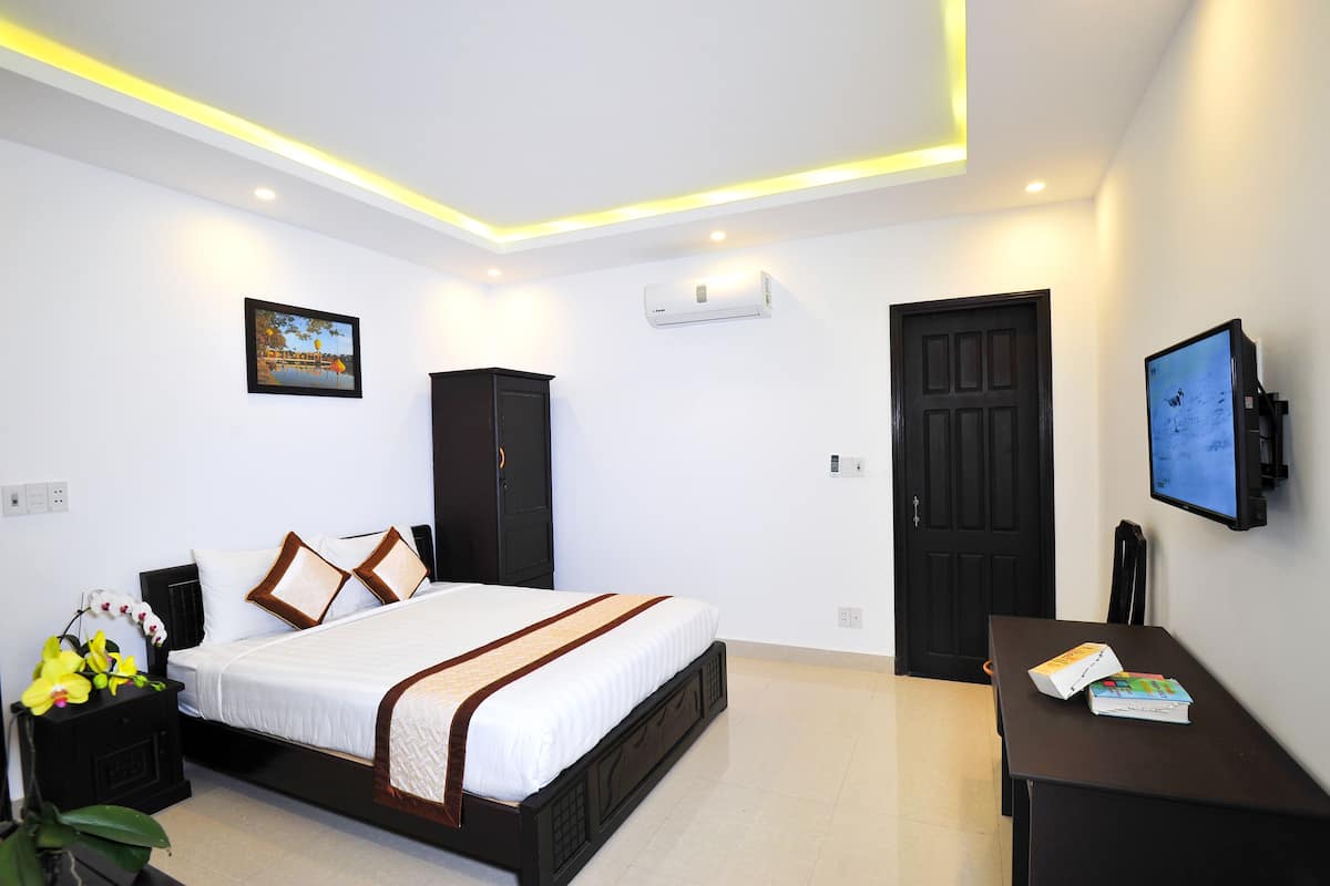 A hotel room with a bed, a desk, a TV, an air conditioner, and a door.