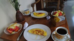 A breakfast setting with an omelette, fruit, coffee, and a vase of flowers. - Hoi An Bali Homestay (Da Nang)