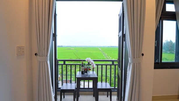 A balcony with a table and chairs, overlooking a green field. - Hoi An Bali Homestay (Da Nang)