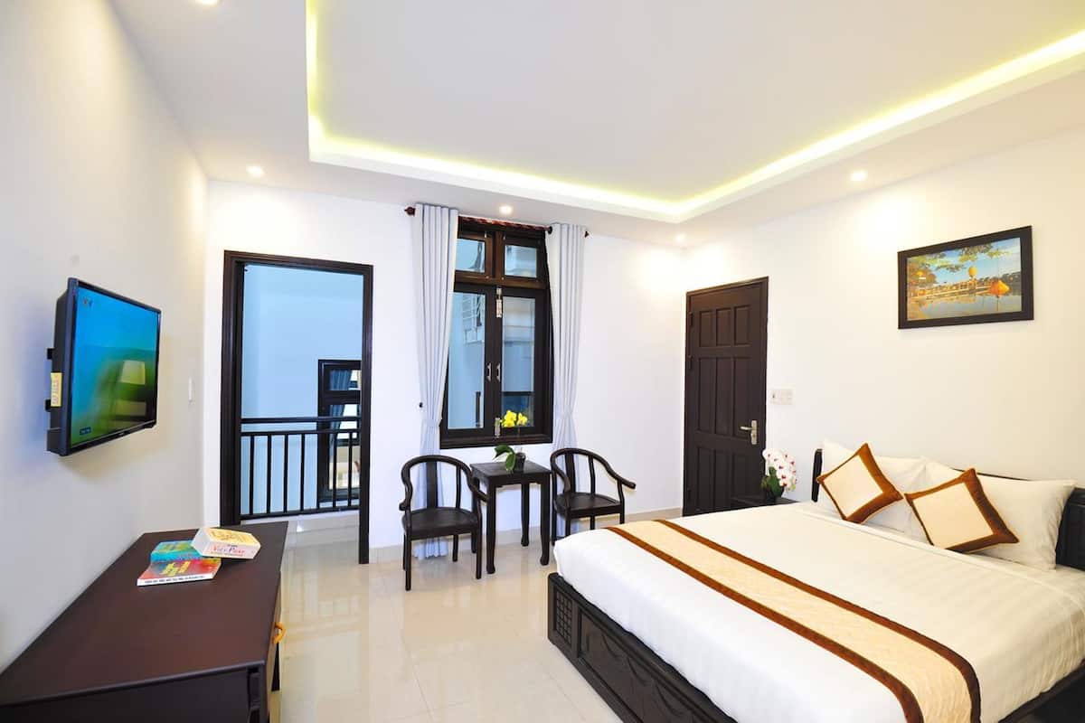 A hotel room with a bed, a desk with a chair, a TV, and a balcony with a view.