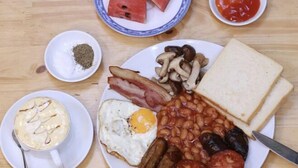 A breakfast plate with toast, eggs, bacon, mushrooms, beans, sausages, tomatoes, and a slice of watermelon. - Hoi An Bali Homestay (Da Nang)