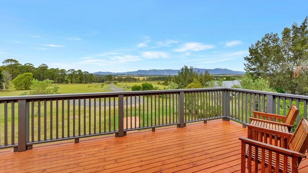 A wooden deck with a view of a green field and mountains in the distance. - Silver Springs Cottage Hunter Valley Retreat (Rothbury)