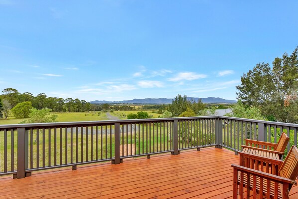 A wooden deck with a view of a green field and mountains in the distance.
