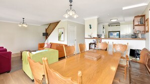 A dining area with a wooden table and chairs, a staircase, and a kitchen area with cabinets and a refrigerator. - Silver Springs Cottage Hunter Valley Retreat (Rothbury)