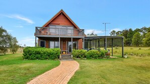 A two-story house with a balcony, a covered porch, and a brick pathway leading to the entrance. - Silver Springs Cottage Hunter Valley Retreat (Rothbury)