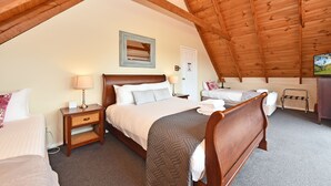 A bedroom with a sloped ceiling, a bed, a bedside table, a lamp, and a wall-mounted TV. - Silver Springs Cottage Hunter Valley Retreat (Rothbury)