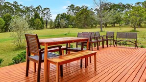 An outdoor wooden deck with a table and chairs, surrounded by a grassy area and trees. - Silver Springs Cottage Hunter Valley Retreat (Rothbury)