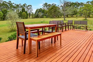 An outdoor wooden deck with a table and chairs, surrounded by a grassy area and trees.