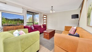 A modern living room with a large flat-screen TV, two sofas, a coffee table, and a ceiling light fixture. - Silver Springs Cottage Hunter Valley Retreat (Rothbury)