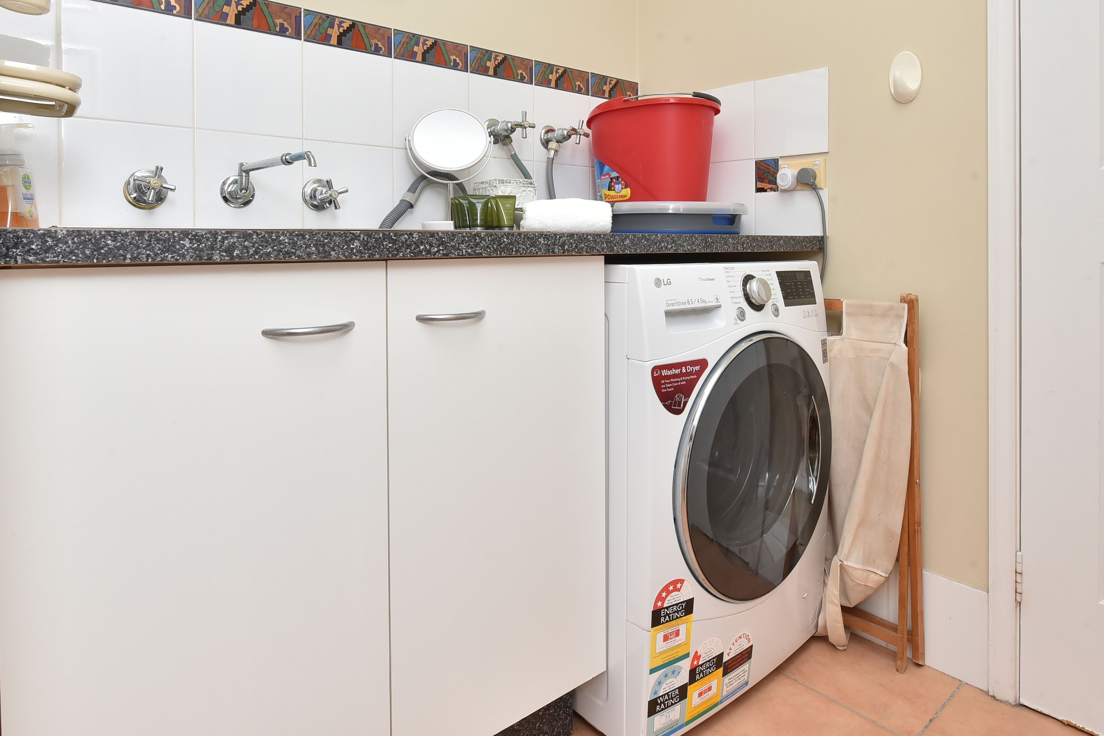 A laundry area with a washing machine, a sink, and a red bucket on the countertop.