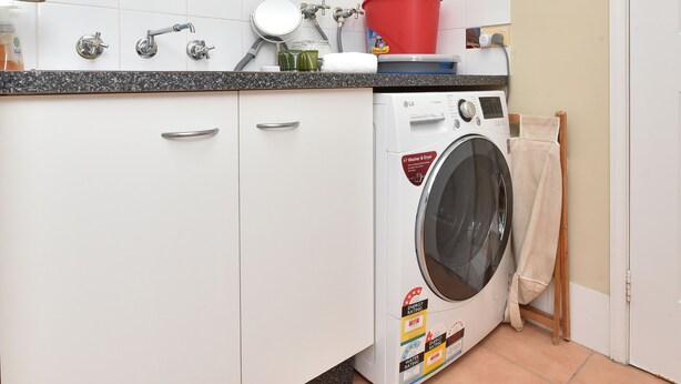 A laundry area with a washing machine, a sink, and a red bucket on the countertop. - Silver Springs Cottage Hunter Valley Retreat (Rothbury)