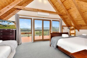 A bedroom with two beds, a wooden ceiling, a balcony with a view, and a dresser.