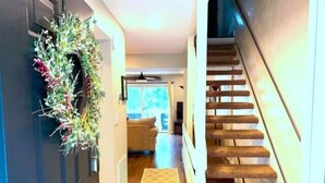 A hallway with a carpeted staircase, a door with a wreath, and a living room in the background. - Shorely Heaven:  WiFi, Disney+, Amazon Prime, YouTubeTV, (2) Kayaks Wide Water Lake Views (Moneta)