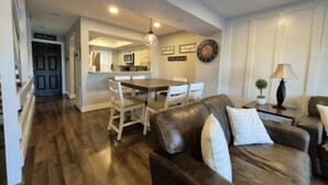 A living room with a brown leather sofa, a dining table with chairs, a kitchen area, and a clock on the wall. - Shorely Heaven:  WiFi, Disney+, Amazon Prime, YouTubeTV, (2) Kayaks Wide Water Lake Views (Moneta)