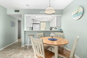 A kitchen with white cabinets, a wooden dining table with chairs, and a hanging light fixture.