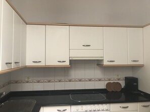 A compact kitchen with white cabinets, a black countertop, and a stove.