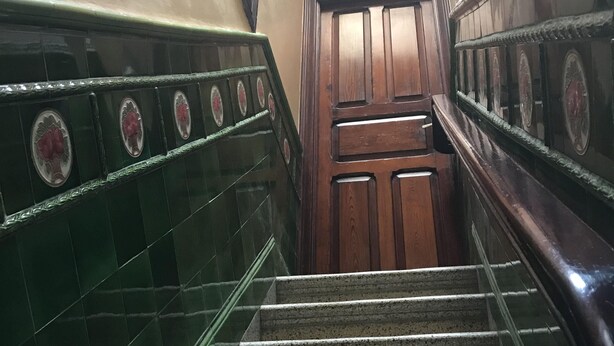 Eine Treppe mit grün gefliesten Wänden und einer Holztür am Oberende.