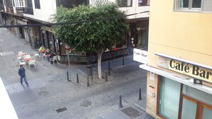 Straßenansicht mit einem Café-Bar, Sitzgelegenheiten im Freien und einem Baum.