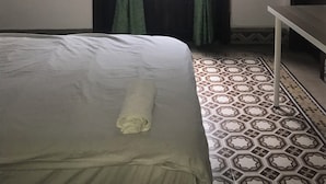 Ein Zimmer mit einem Bett, einem Vorhangfenster, einem Tisch und einem gemusterten Boden.