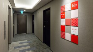 A hotel hallway with a ceiling light, a wall-mounted emergency exit sign, and a series of red and white directional signs on the wall. - HOTEL M’s EST KYOTO STATION SOUTH (Kyoto)