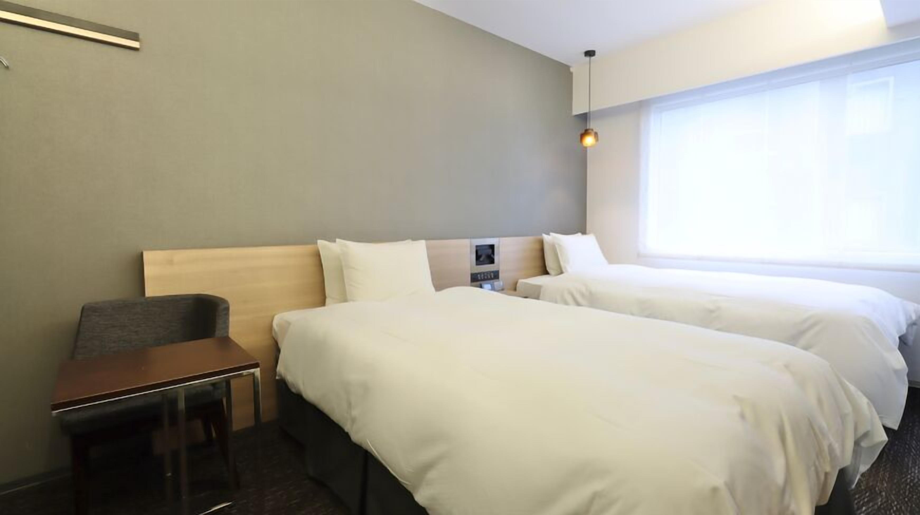 A hotel room with two beds, a desk, a chair, and a large window.
