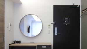 A modern hotel room with a round mirror, a black door with an emergency exit sign, a minibar with beverages, and a small desk with a telephone and a notepad. - HOTEL M’s EST KYOTO STATION SOUTH (Kyoto)