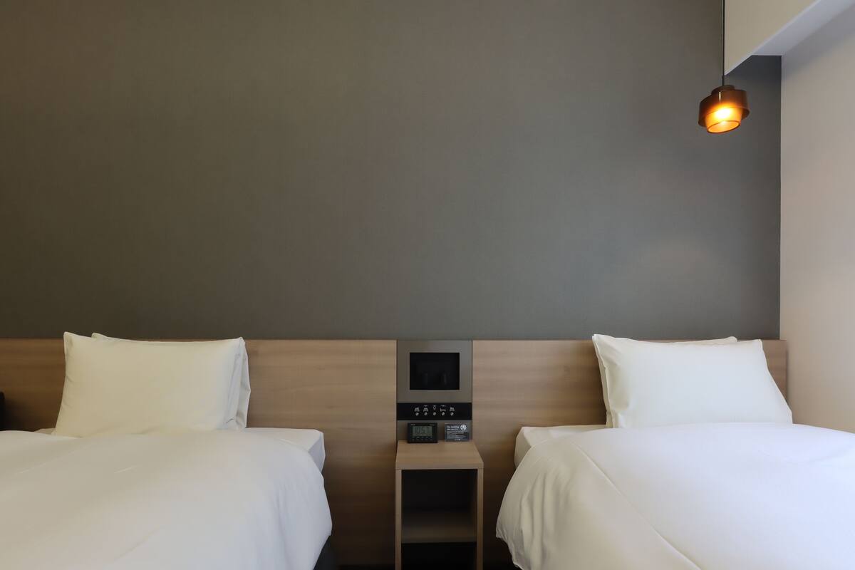 Une chambre d’hôtel avec deux lits, une table de chevet avec une horloge et un luminaire fixé au mur.