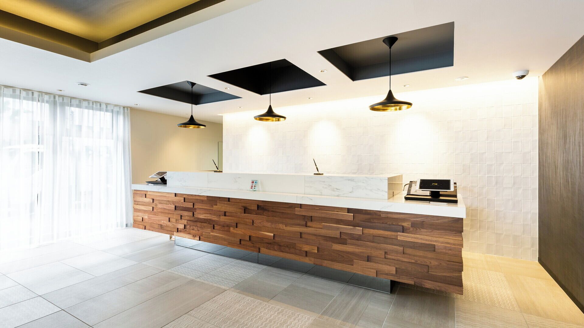 A modern reception area with a wooden counter, pendant lights, and a tiled wall.