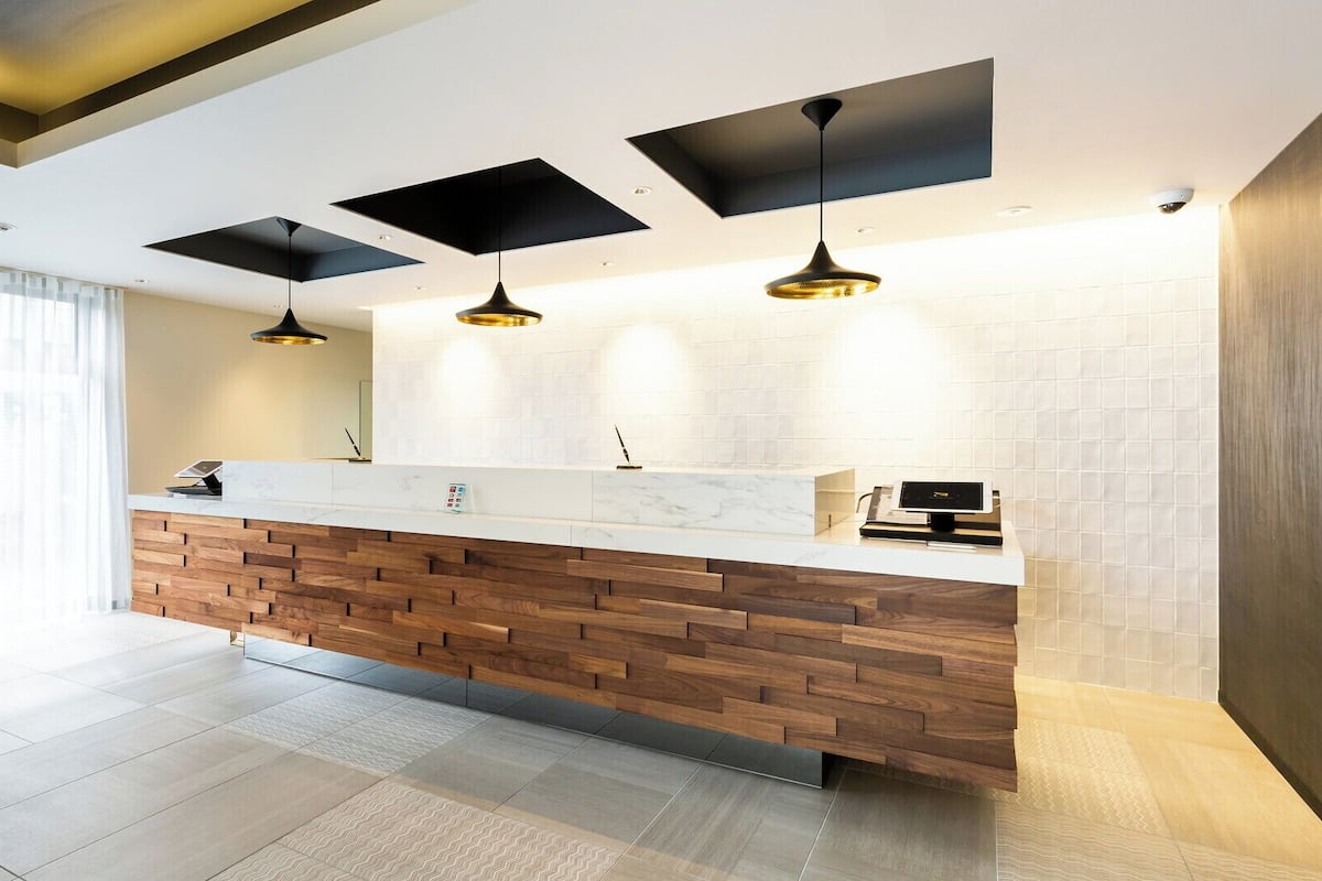Un espace d’accueil moderne avec un comptoir en bois, des luminaires suspendus et un mur recouvert de carreaux.