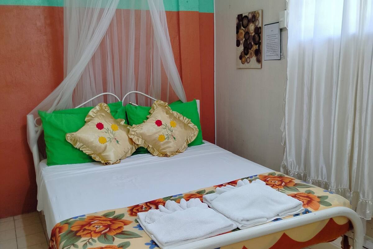 A bed with a floral bedspread, green and beige pillows, and a white canopy.