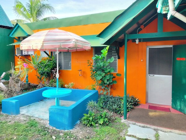 A small outdoor area with a blue seating area, a striped umbrella, and various plants.