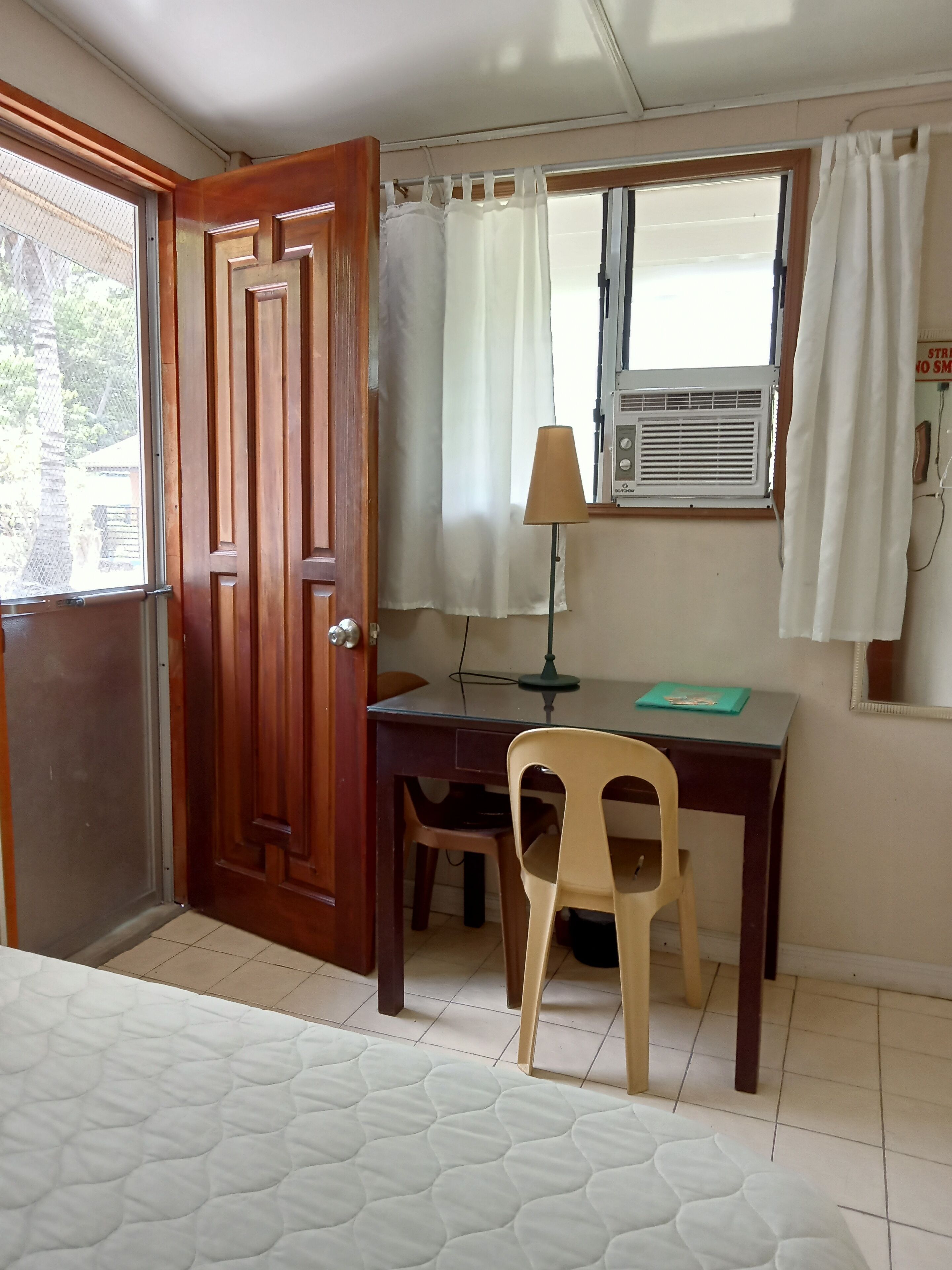 Une pièce avec une porte en bois, un bureau avec une lampe, une chaise et une fenêtre avec des rideaux.