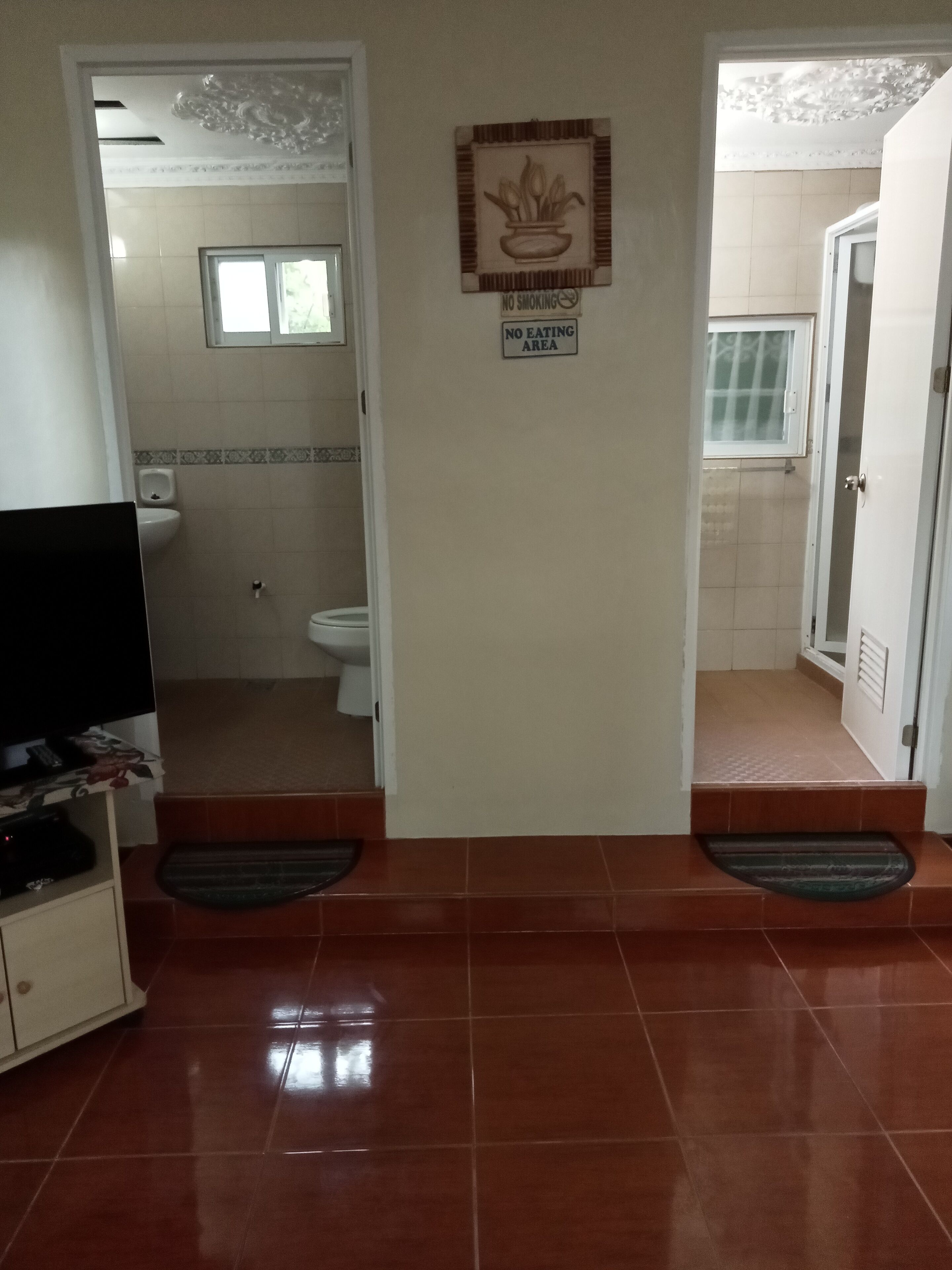 A hotel lobby with a television on a stand, a sign indicating a no smoking and no eating area, and a tiled floor.