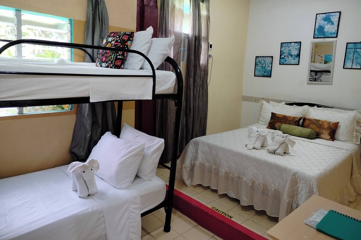 A dormitory room with bunk beds, a single bed, and a desk with a notebook.