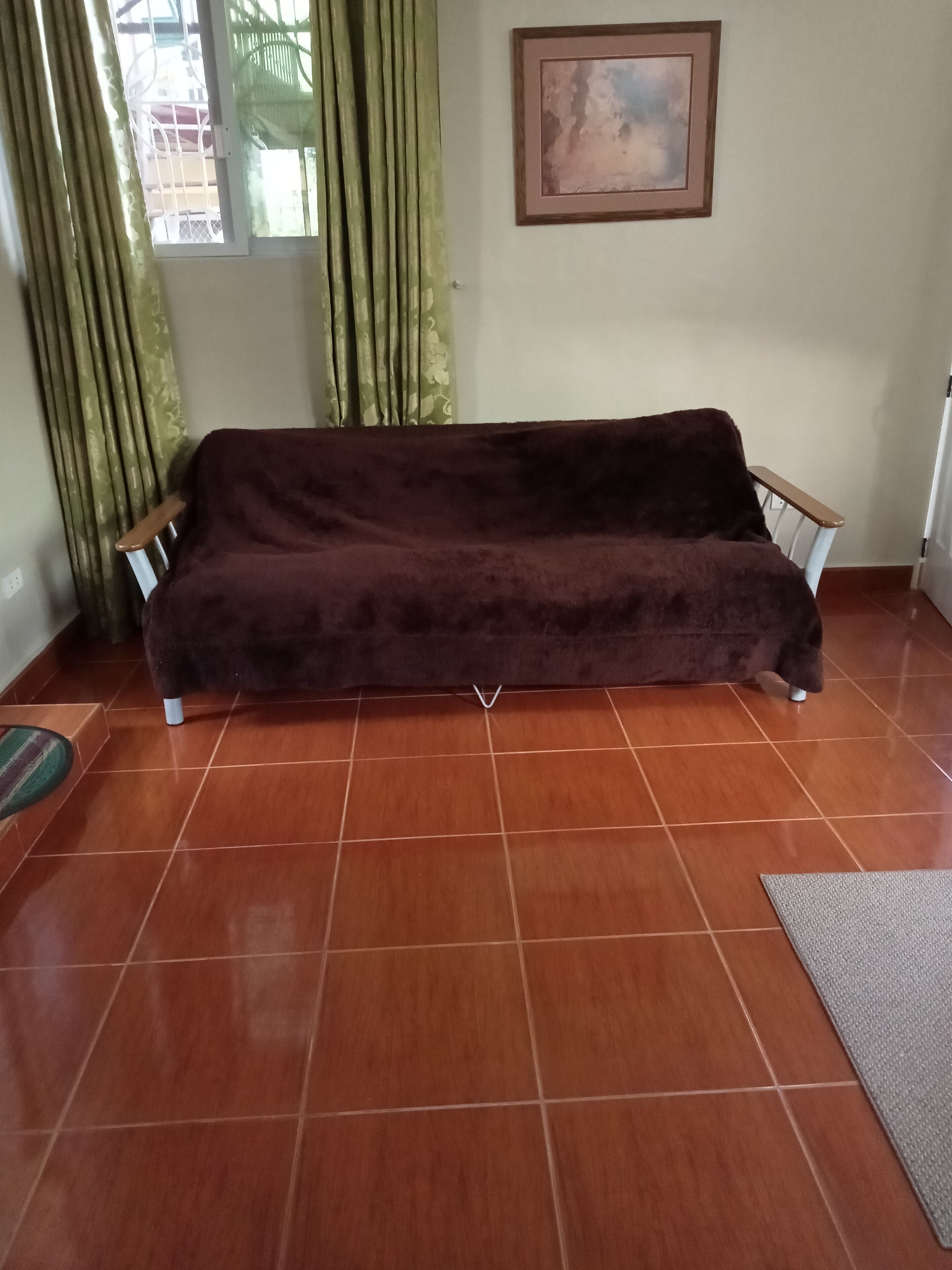 Una habitación con un sofá marrón oscuro, un cuadro en la pared y una ventana con cortinas.