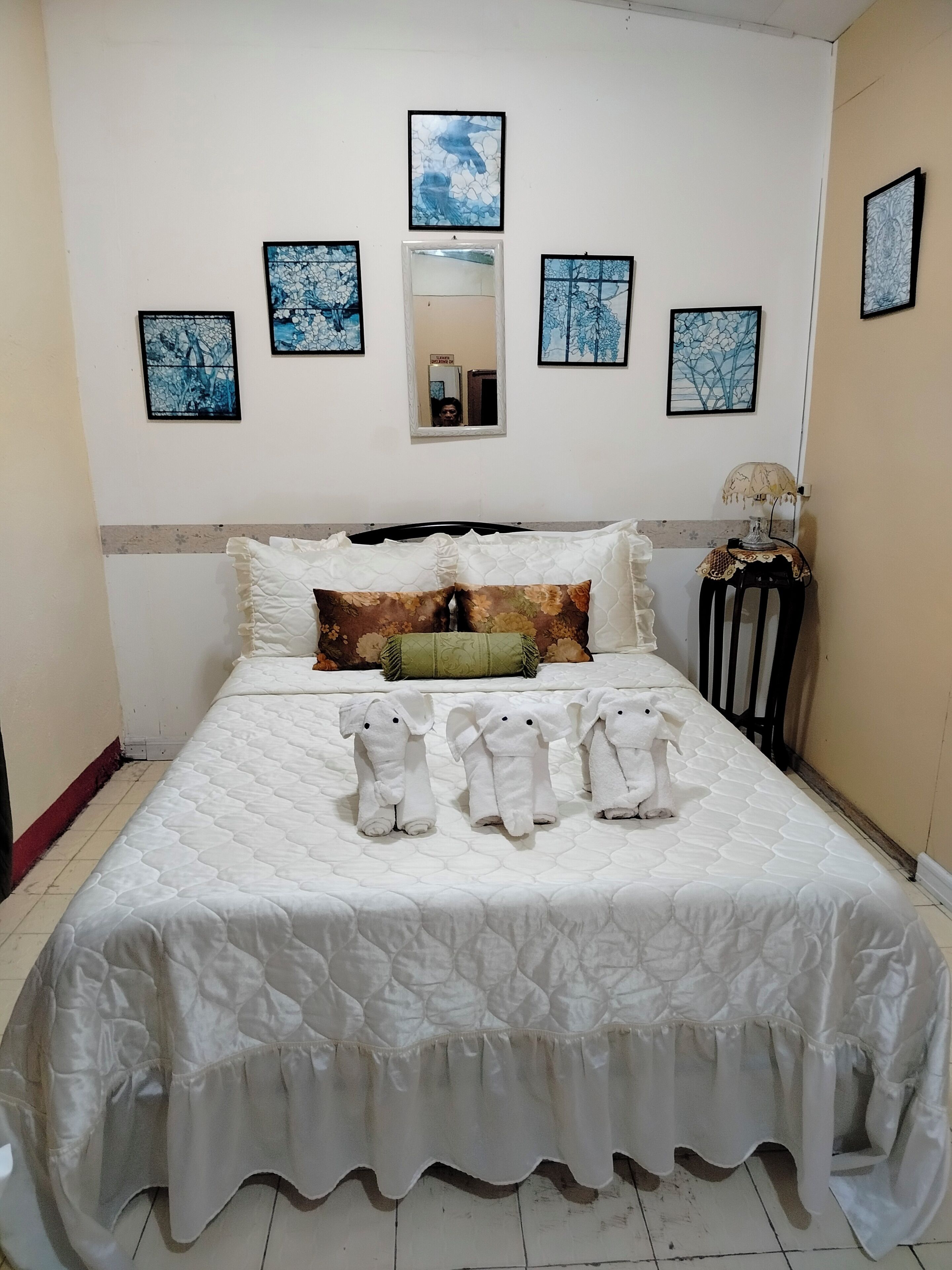 Ein ordentlich gemachtes Bett mit weißer Decke, einem Spiegel und mehreren gerahmten Kunstwerken an der Wand.