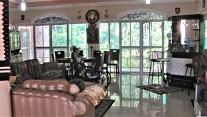 A spacious living room with a large window, a sofa, a dining table, and a kitchen area. - Villa 301 B&B (Baclayon)