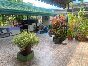 A covered outdoor area with tiled flooring, potted plants, a bench, and a motorcycle. - Villa 301 B&B (Baclayon)