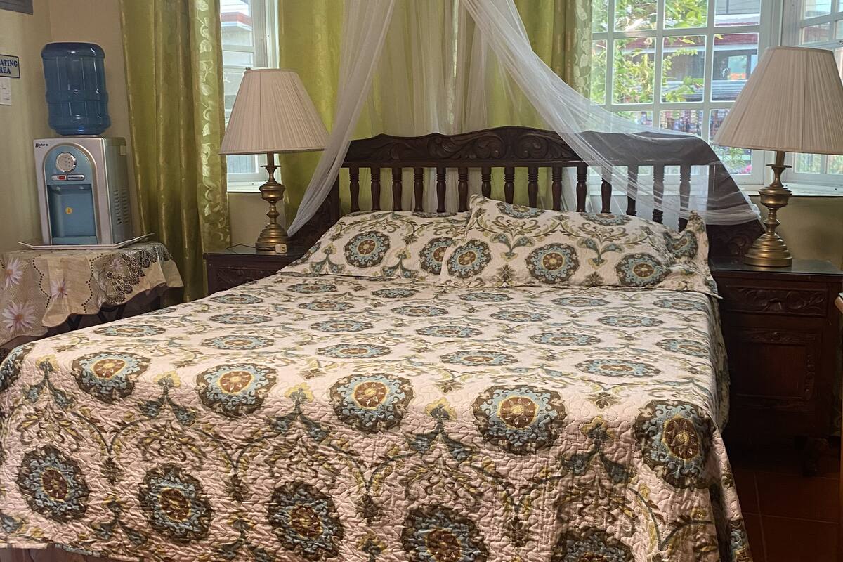 A bedroom with a four-poster bed, green curtains, a water dispenser, and two bedside lamps.