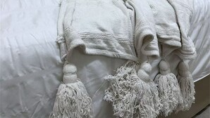 Un llit ben arropat amb unaCoberta blanca i una manta decorativa amb borlons.