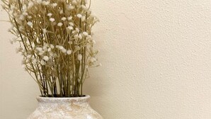 Un vas amb flors seques, un petit pot amb l'etiqueta 'Vanilla & Jasmine', i una garlandes de nines de fusta damunt d'una taula rodona.