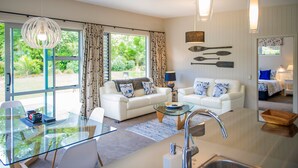 A modern living room with a glass coffee table, white sofas, and a dining area with a glass table.