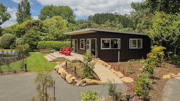 Una cabaña moderna con porche cubierto, rodeada de un jardín cuidado y un bosque de fondo.