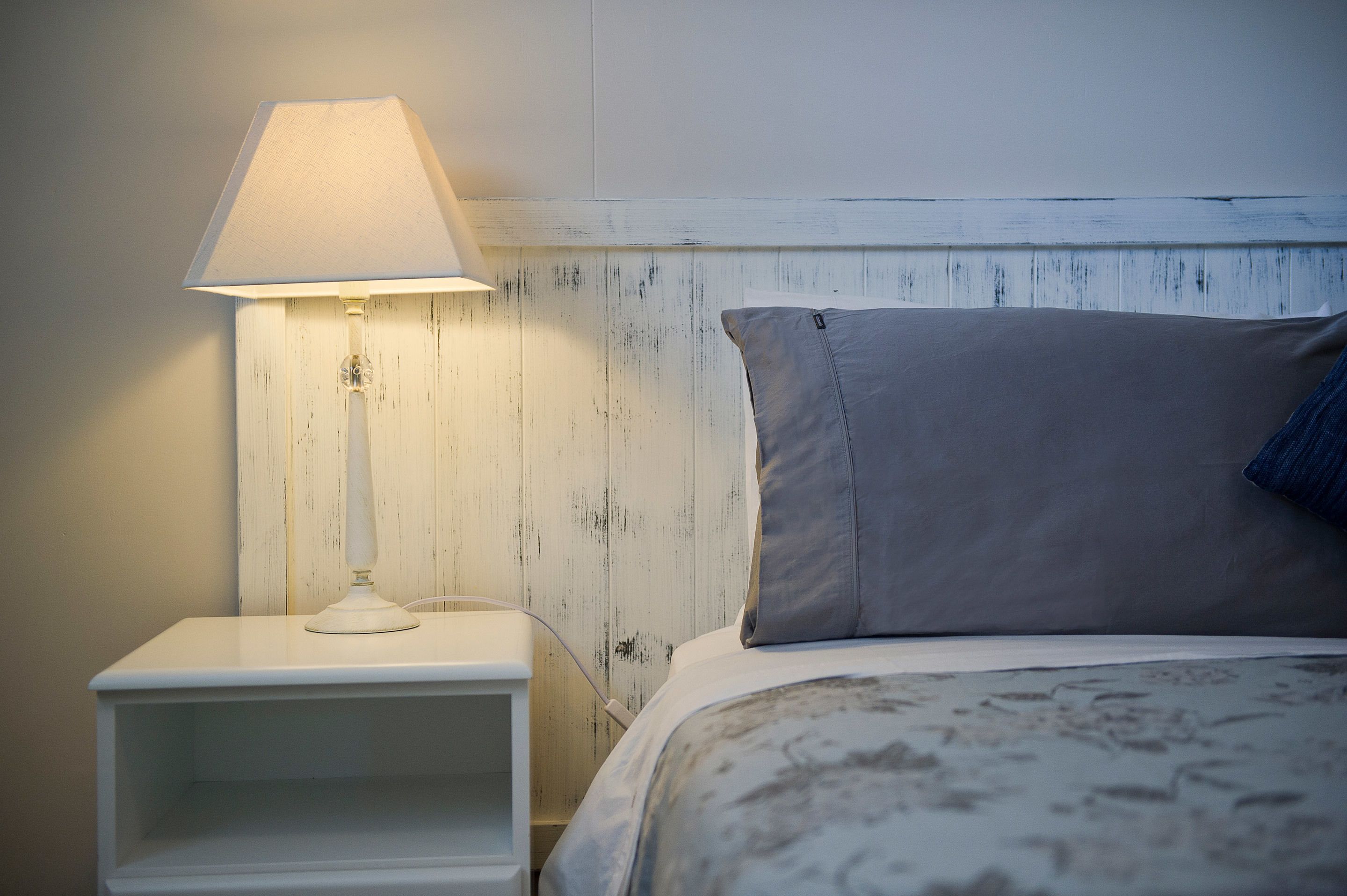 A neatly made bed with a pillow and a bedside lamp on a white nightstand.