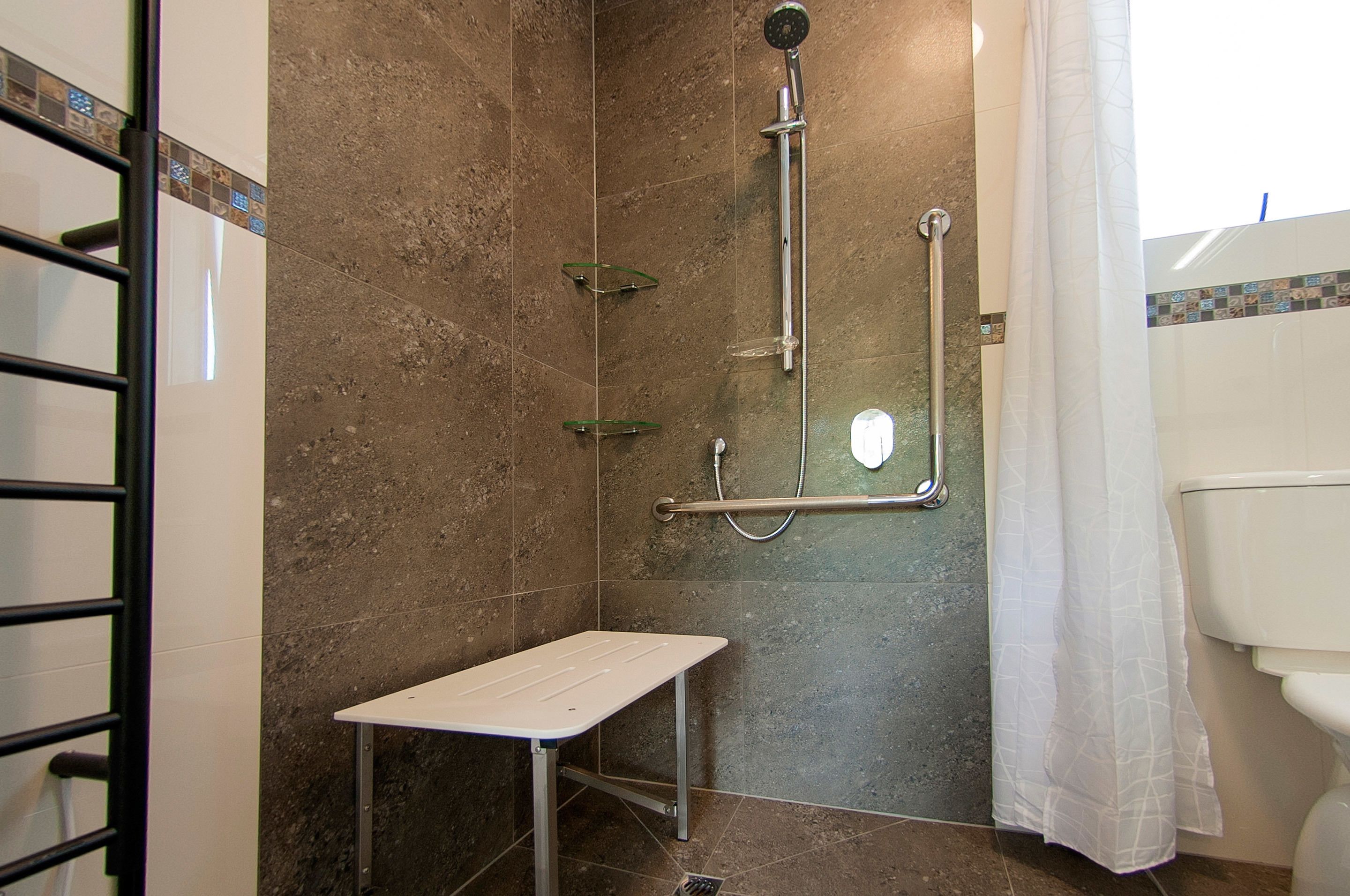 A shower area with a glass shelf, a handheld showerhead, and a grab bar.