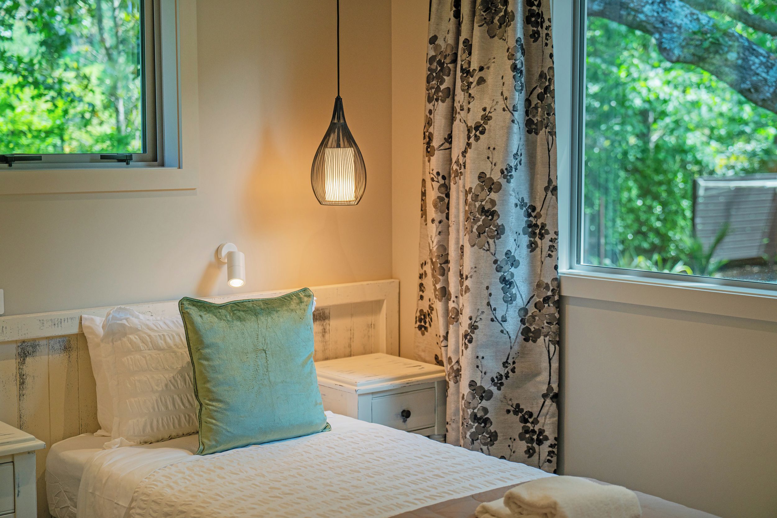 A bedroom with a bed, a nightstand, a wall-mounted lamp, and a window with curtains.